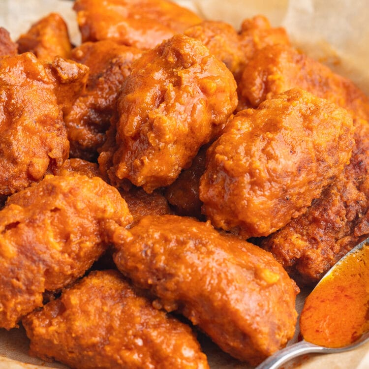 Side view of a pile of orange-sauced buffalo boneless chicken wings in a bowl.