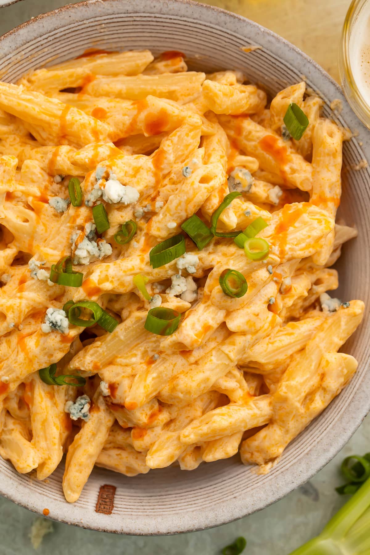 Close-up of an off-white bowl holding creamy buffalo chicken alfredo made with penne pasta and topped with sliced green onions.