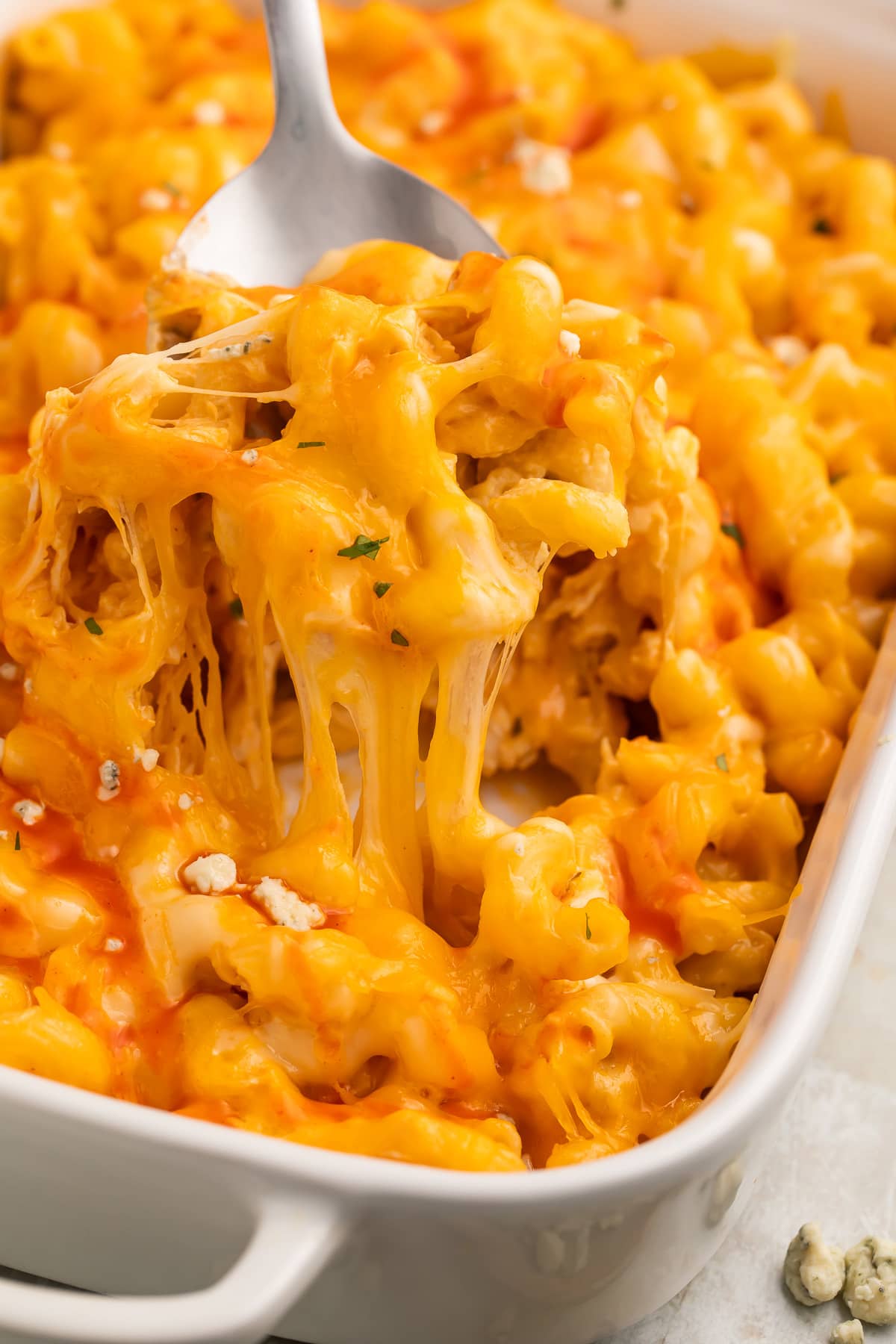 A large spoonful of orange buffalo chicken mac and cheese being lifted out of a casserole dish.