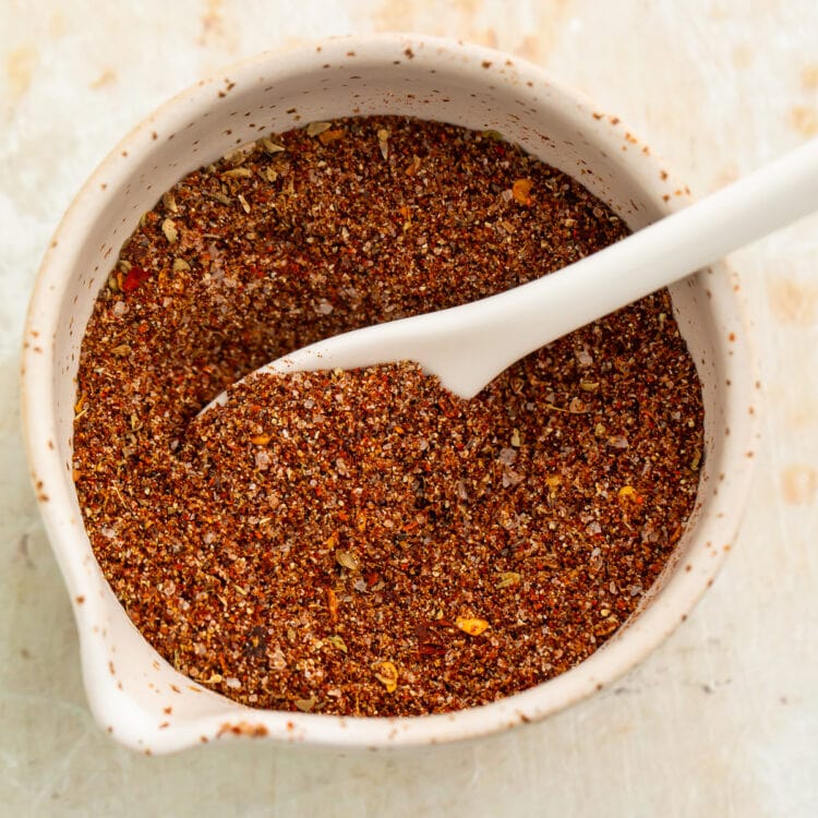 Overhead view of a small bowl filled with a rich, deep reddish-brown blend of spices for chicken taco seasoning.