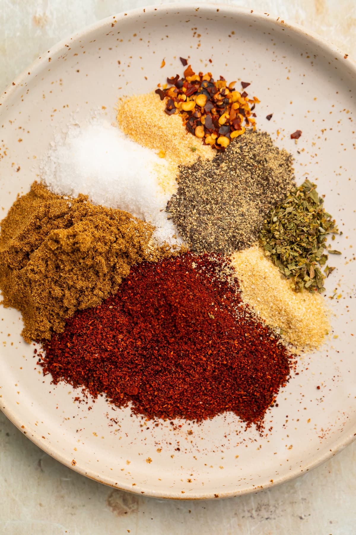 Overhead view of all spices needed for chicken taco seasoning on a neutral plate.