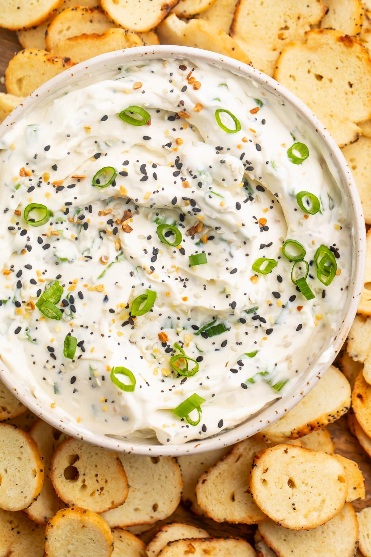Overhead view of a bowl of Everything Bagel dip topped with Everything Bagel seasoning and green onions.