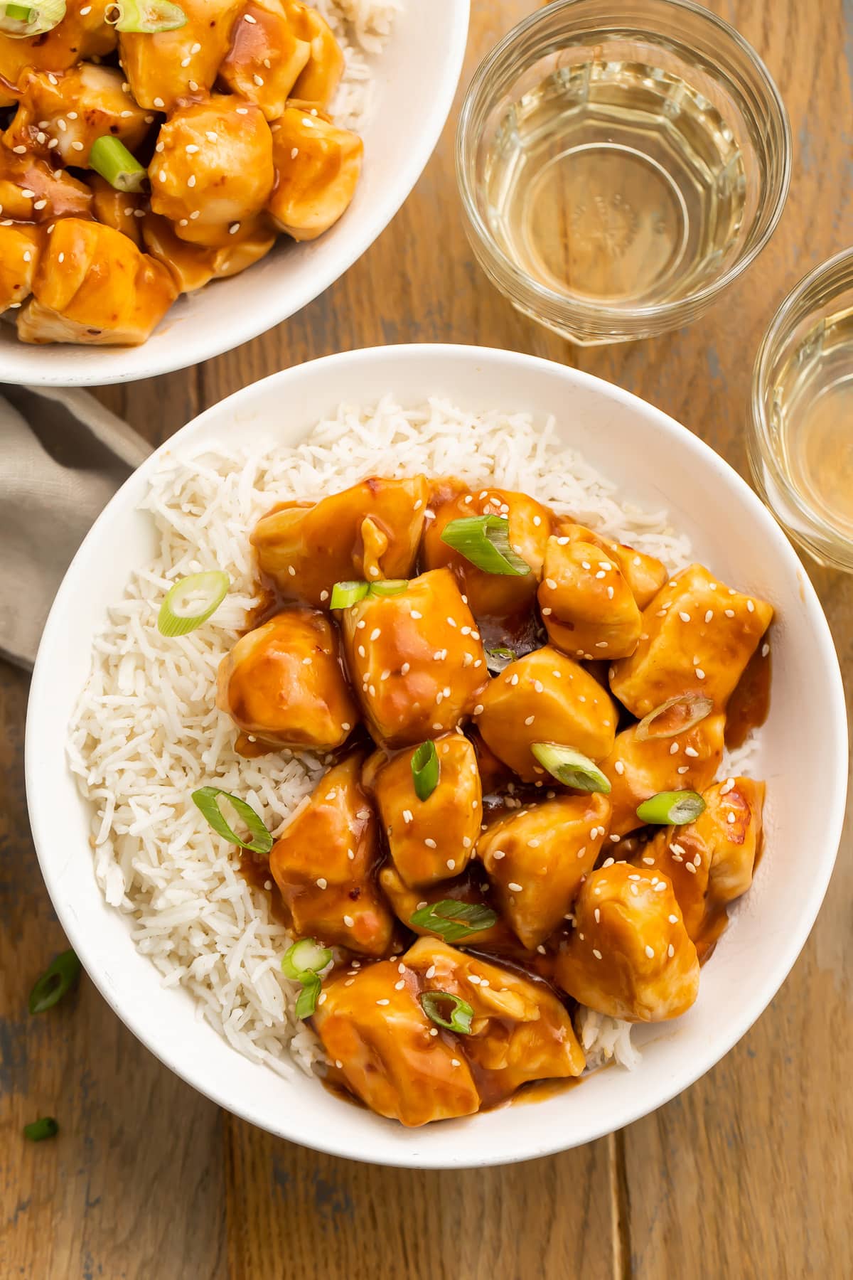 Orange glazed Instant Pot honey garlic chicken garnished with sesame seeds and sliced green onions in a bowl with white rice.