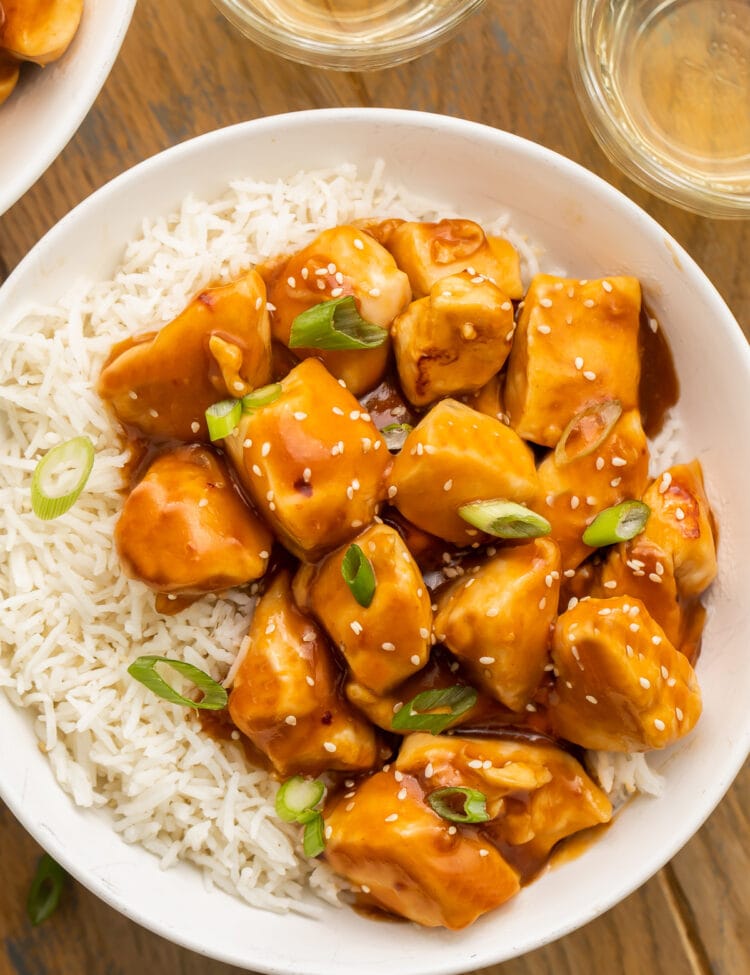 Orange glazed Instant Pot honey garlic chicken garnished with sesame seeds and sliced green onions in a bowl with white rice.