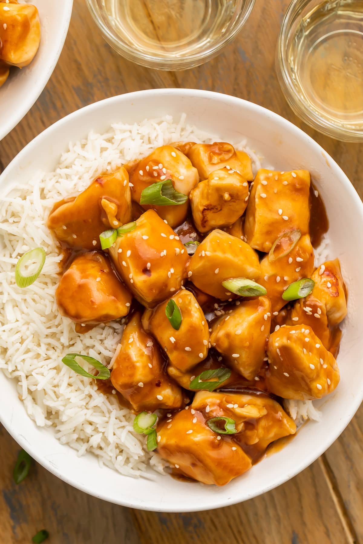Orange glazed Instant Pot honey garlic chicken garnished with sesame seeds and sliced green onions in a bowl with white rice.