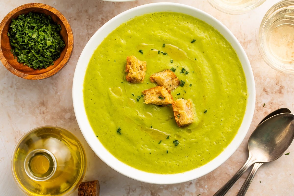 A bowl of bright green zucchini soup on a table.
