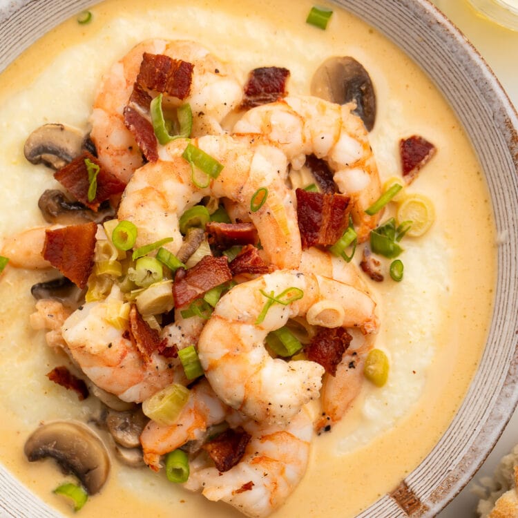 Overhead view of a large white bowl holding creamy grits topped with pink shrimp, bacon, and mushrooms.