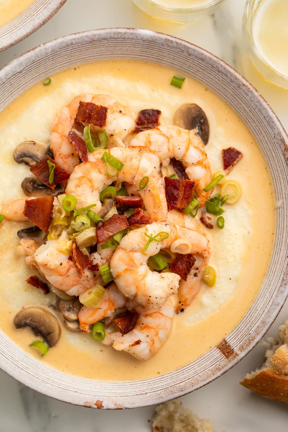 Overhead view of a large white bowl holding creamy grits topped with pink shrimp, bacon, and mushrooms.