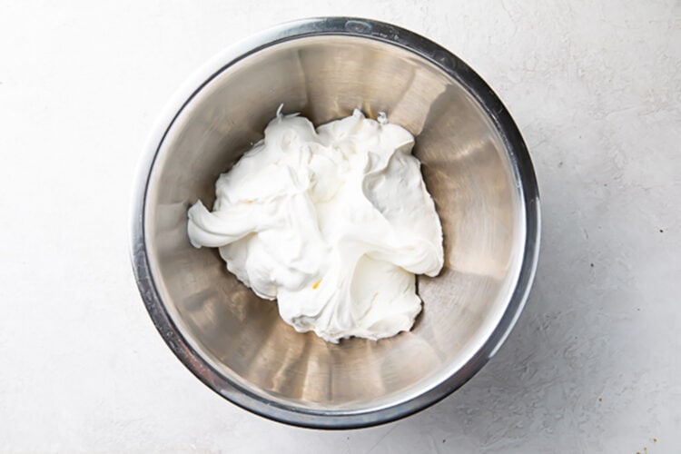 Cream cheese and confectioners' sugar in a large silver mixing bowl.