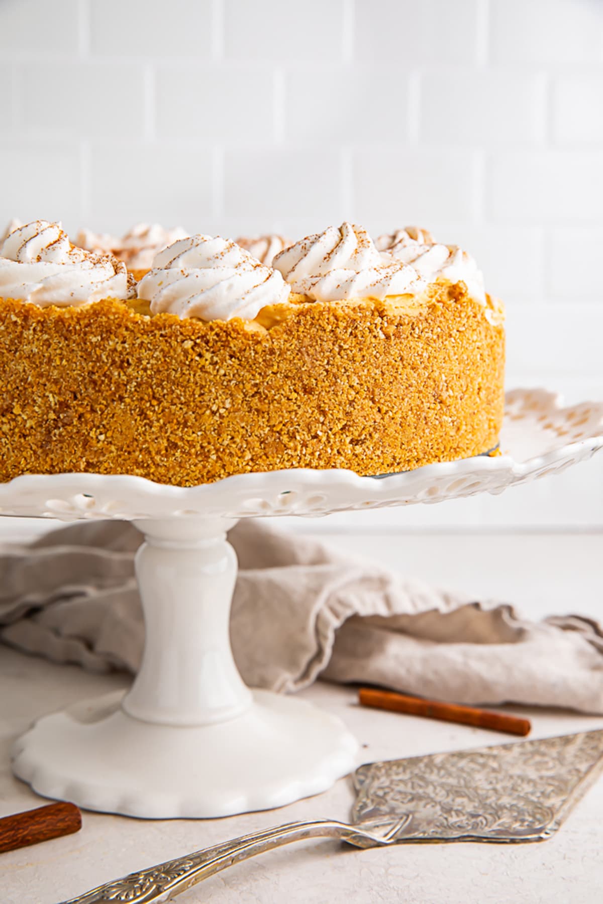 Side view of a whole no bake pumpkin cheesecake on a white cake stand, showing off the side of the crust.