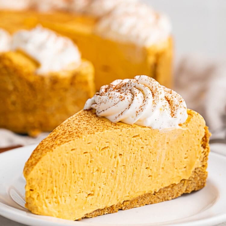 A slice of no bake pumpkin cheesecake topped with a dollop of whipped cream on a white plate.