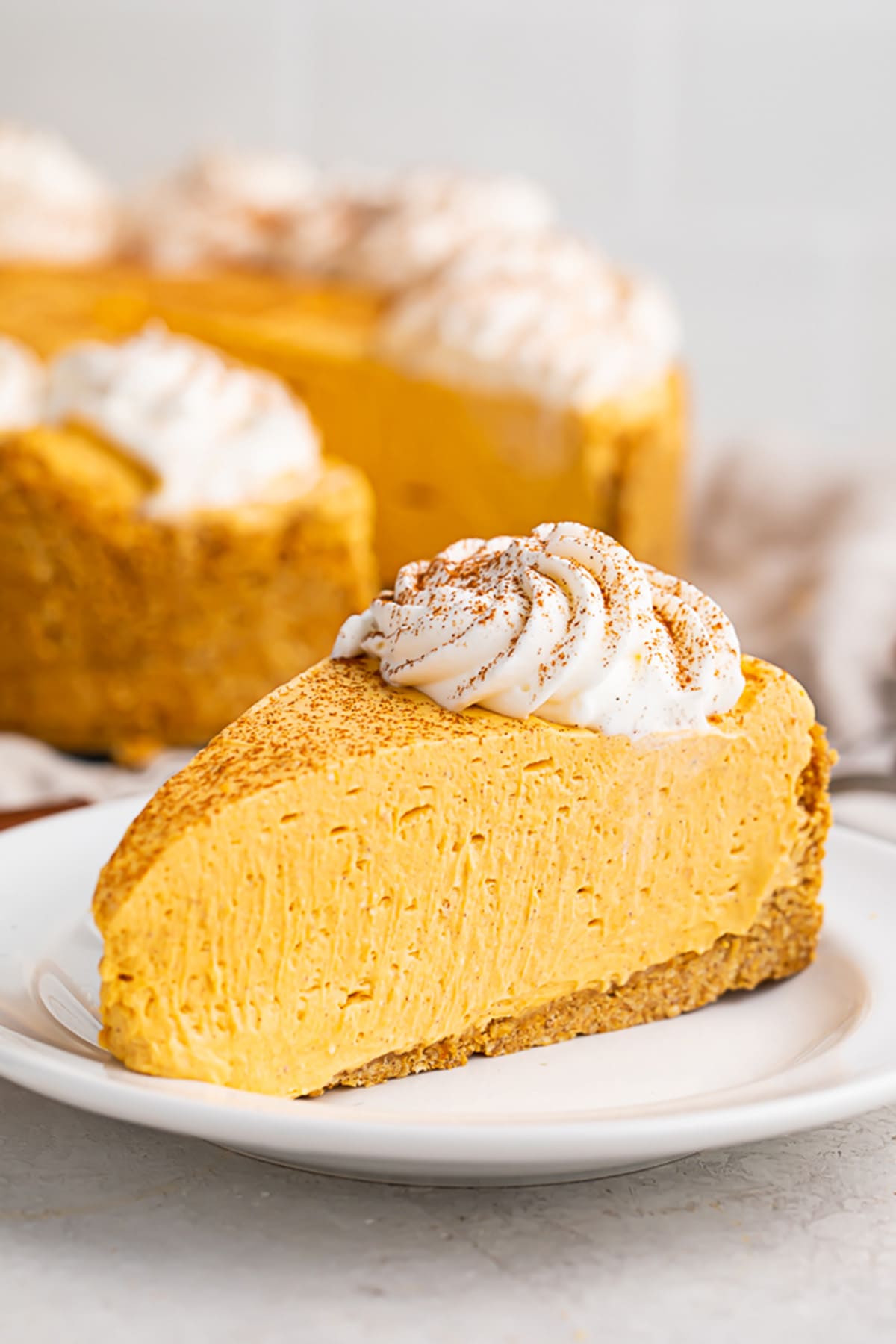 A slice of no bake pumpkin cheesecake topped with a dollop of whipped cream on a white plate.