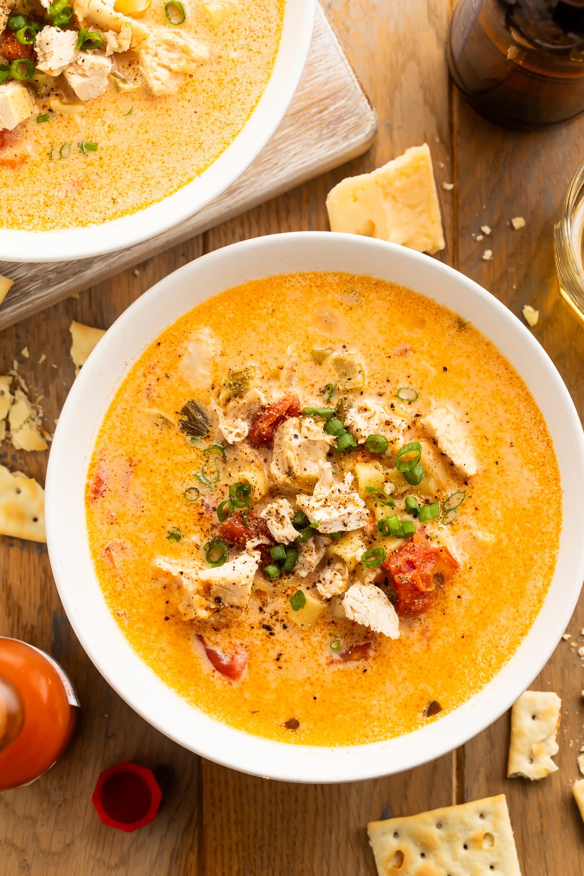 Overhead view of a bowl of Instant Pot cajun chicken pasta soup on a dark wooden table surrounded by broken saltine crackers.