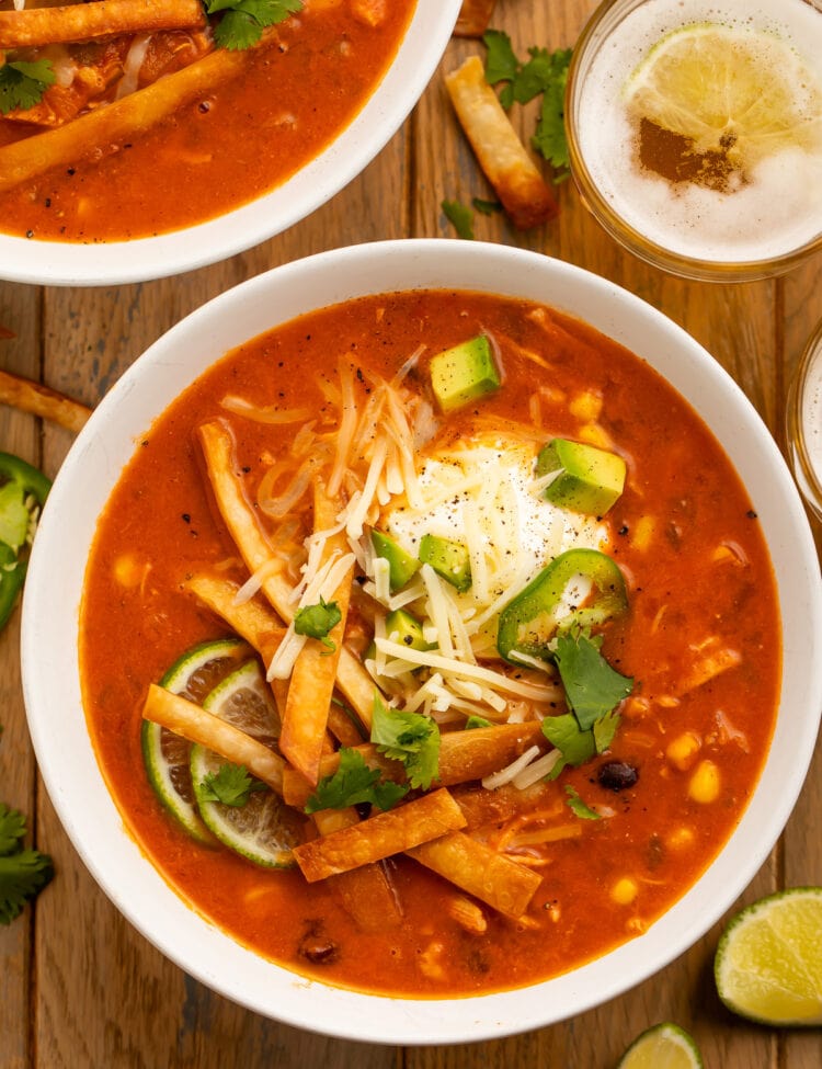 Overhead photo of a large white bowl holding deep red chicken tortilla soup, made in an Instant Pot, topped with tortilla strips, cheese, avocado, and cilantro.