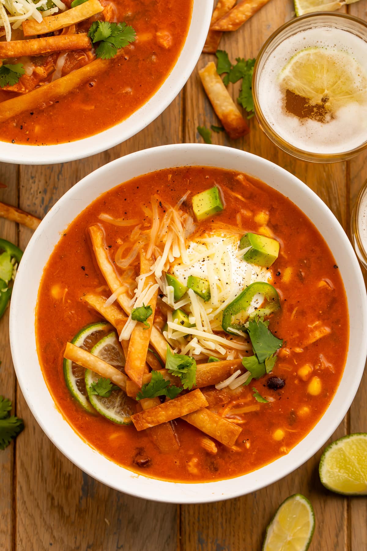 Overhead photo of a large white bowl holding deep red chicken tortilla soup, made in an Instant Pot, topped with tortilla strips, cheese, avocado, and cilantro.