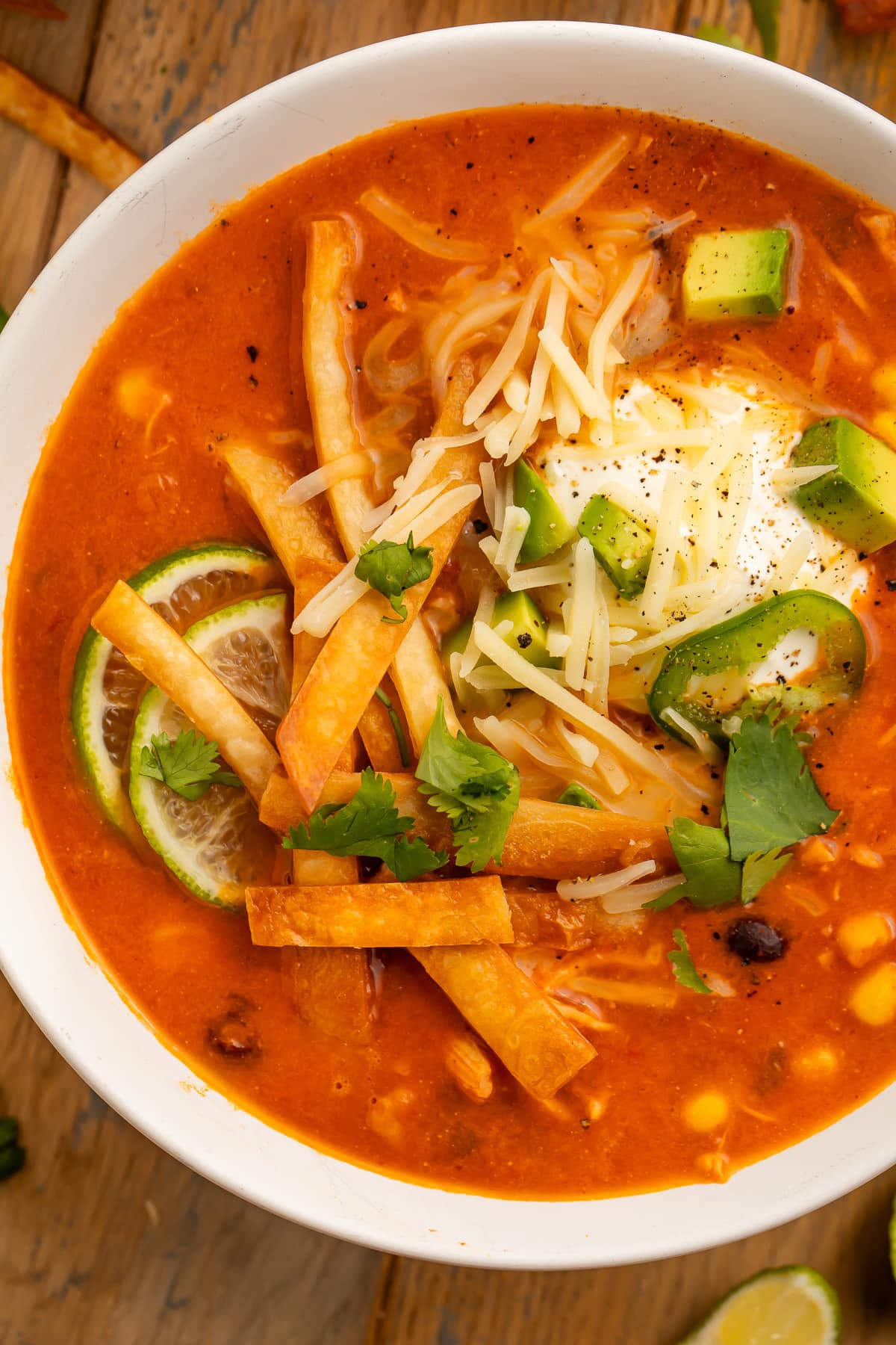 Close-up photo of a large white bowl holding deep red chicken tortilla soup, made in an Instant Pot, topped with tortilla strips, cheese, avocado, and cilantro.