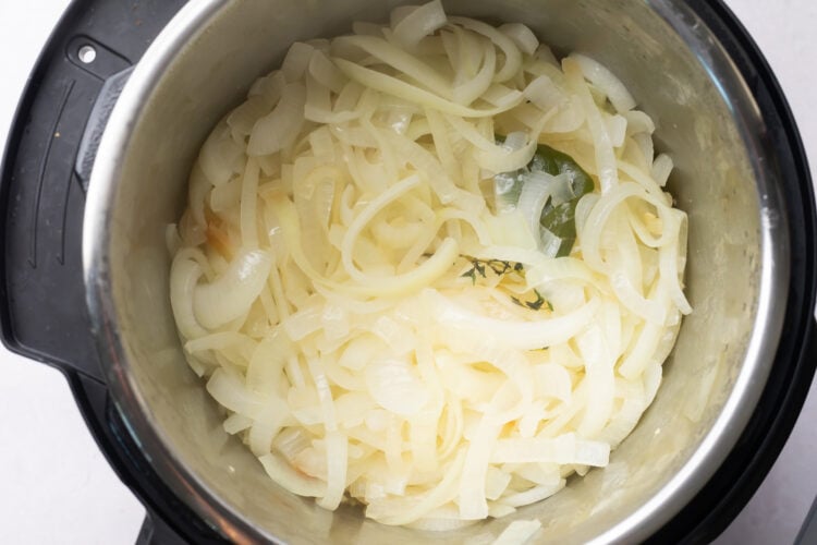 Sliced, softened onions in the bottom of an Instant Pot.