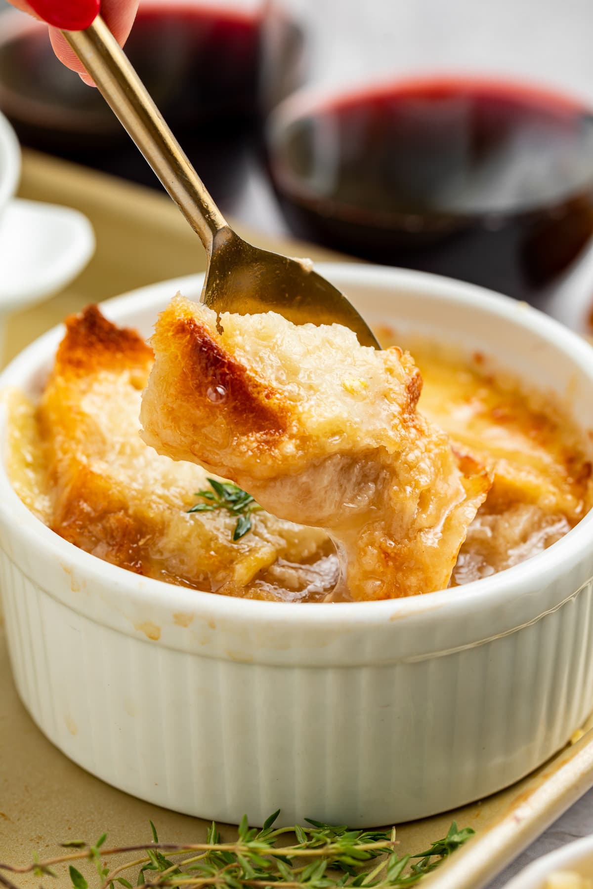A spoon lifting a piece of French bread off the top of a ramekin holding Instant Pot French onion soup.