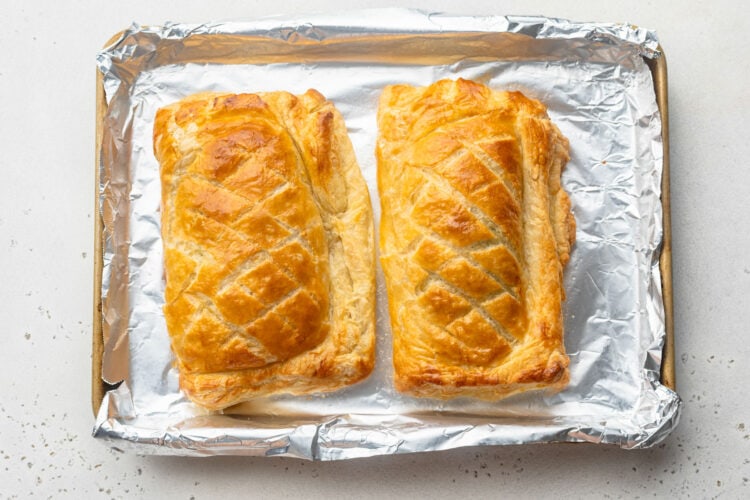 Fully baked, golden brown Salmon Wellingtons, scored with crosshatch patterns, on a baking sheet lined with parchment paper.