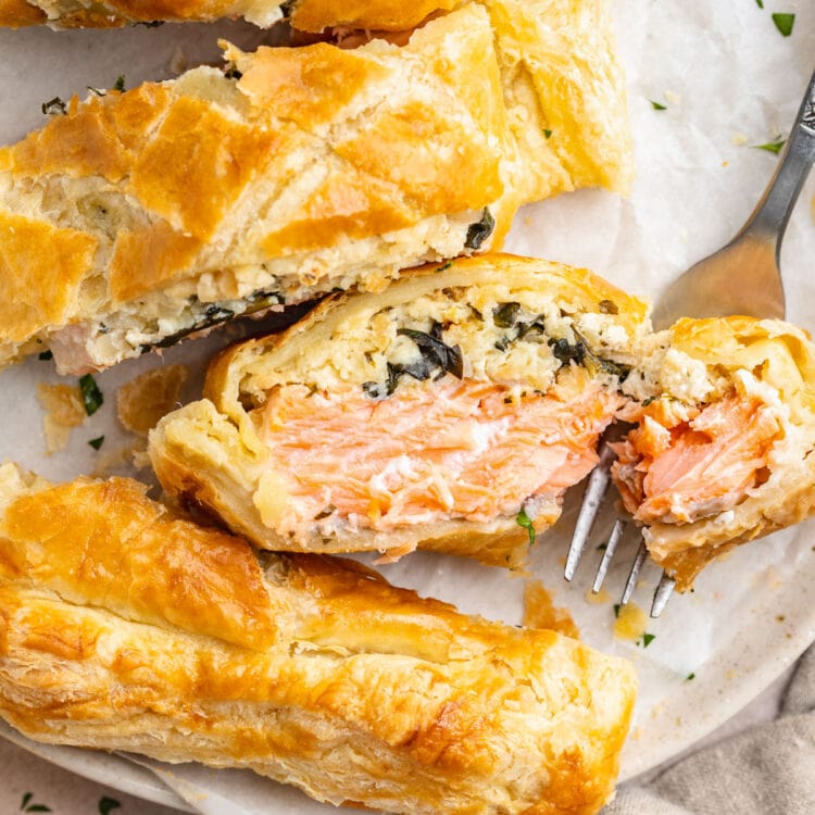 Salmon wellington, sliced and plated on a white round plate, with one slice placed on its side to show the salmon filling.