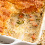 Chicken pot pie casserole in a square dish, with a corner scooped out to show some of the filling.