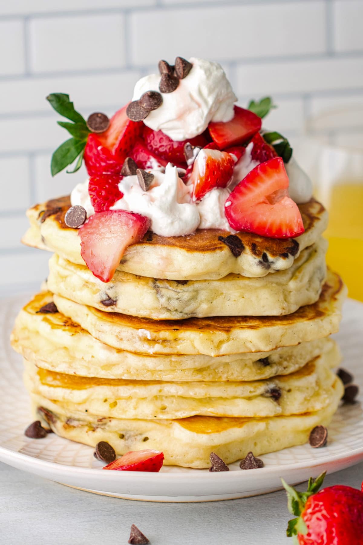 A stack of chocolate chip pancakes topped with whipped cream and sliced strawberries.