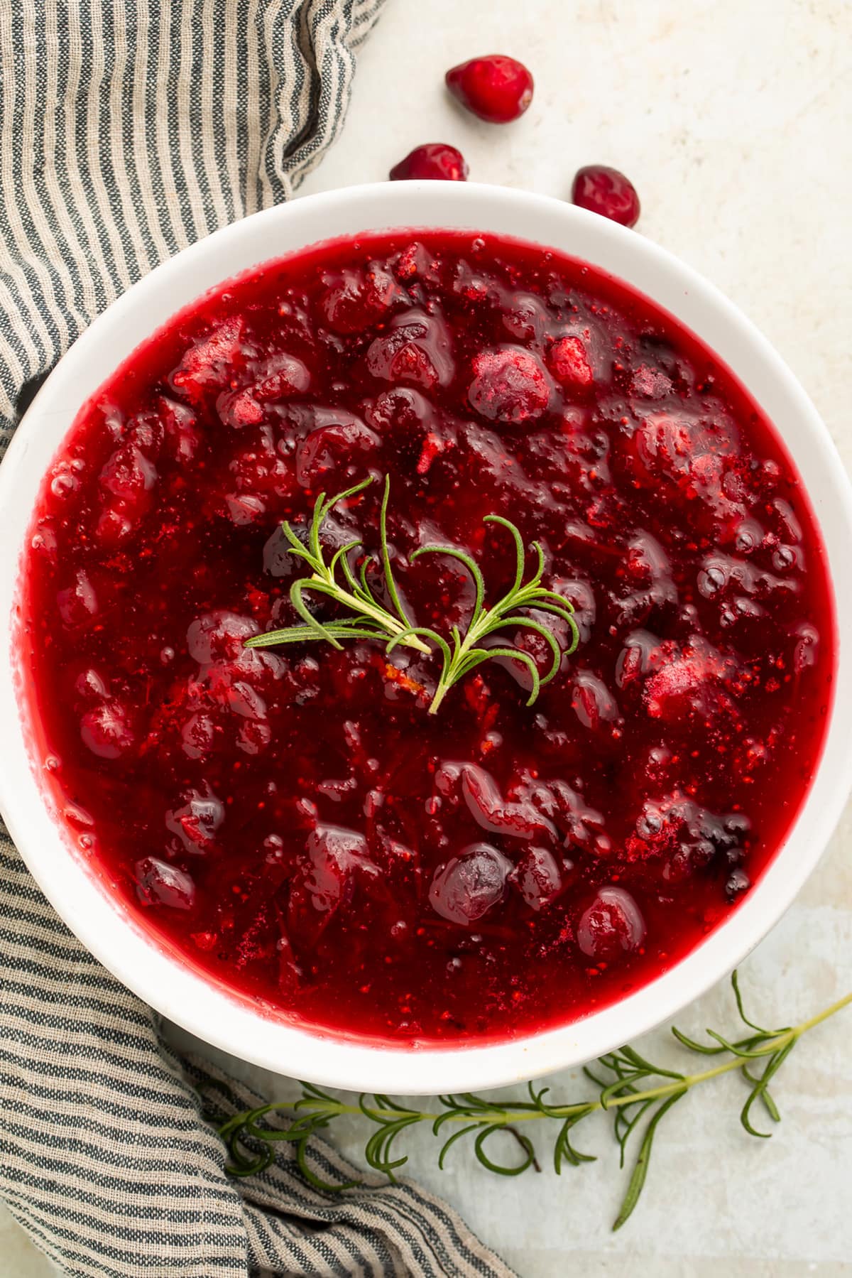 Overhead photo of whole berry rosemary cranberry sauce in a white bowl with a garnish of fresh rosemary.