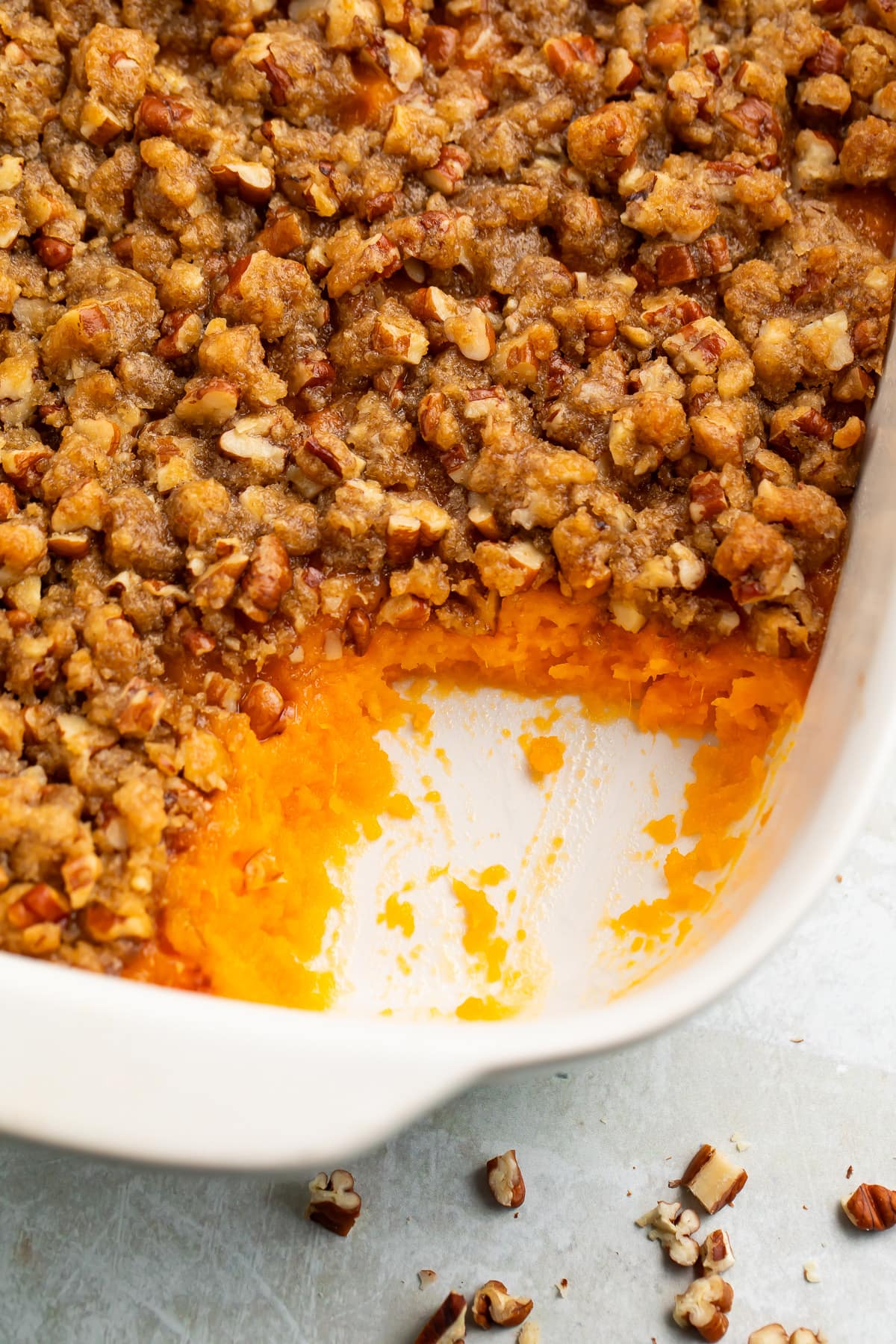 A casserole dish of Ruth's Chris sweet potato casserole topped with pecans and brown sugar, with a scoop of casserole missing from the corner of the dish.