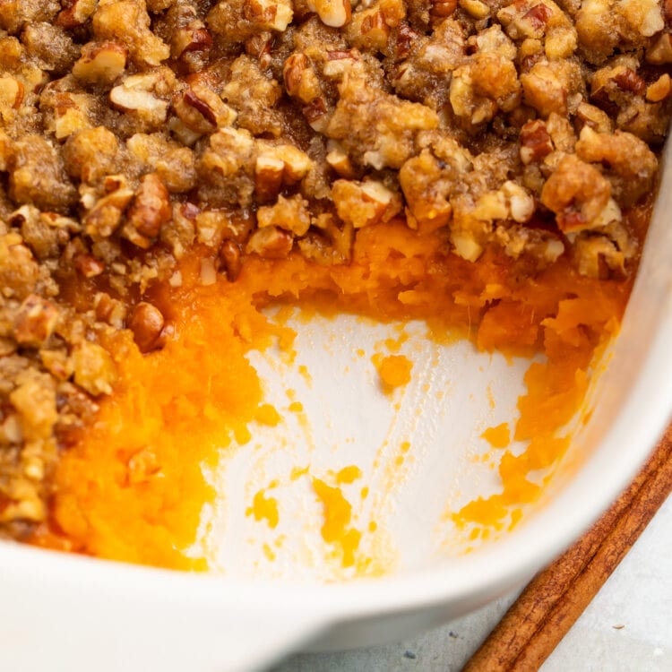 A casserole dish of Ruth's Chris sweet potato casserole topped with pecans and brown sugar, with a scoop of casserole missing from the corner of the dish.