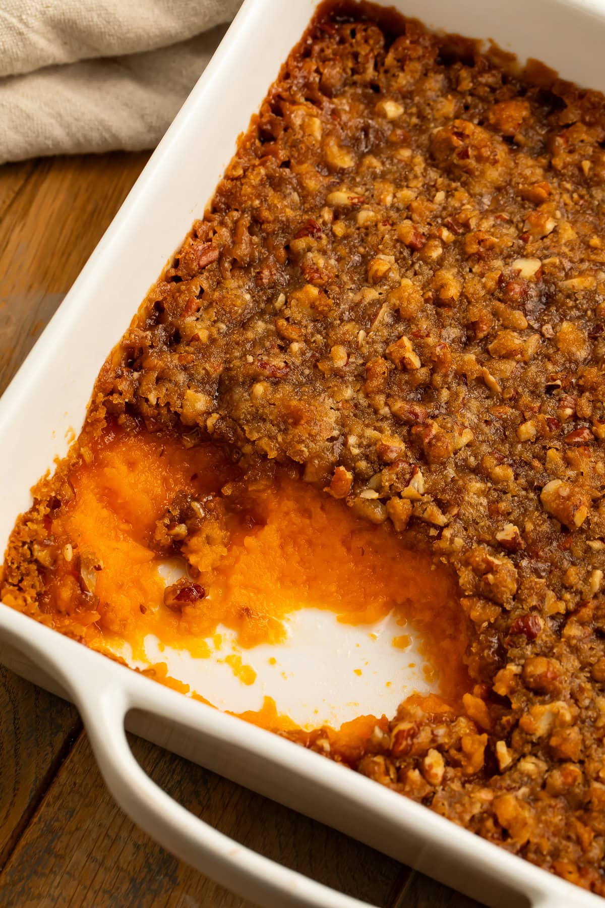 Close up of a sweet potato casserole with a spoonful missing, and a crunchy pecan praline topping.