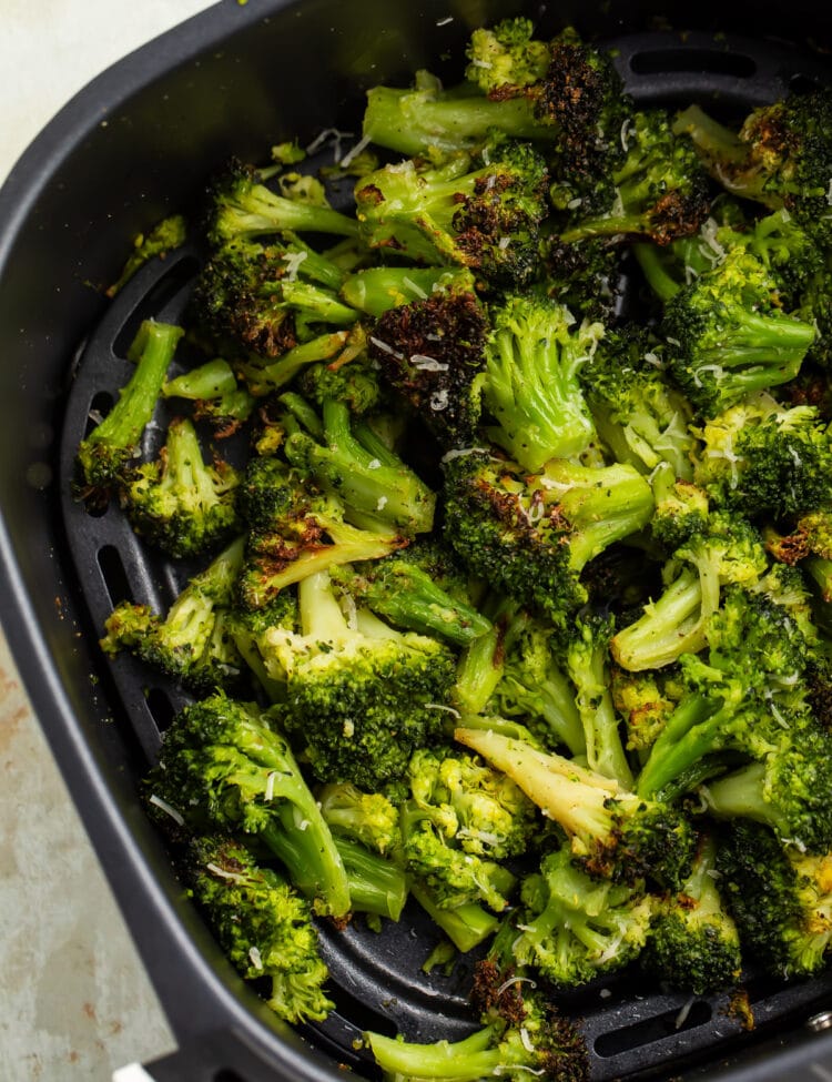 Previously frozen broccoli florets, resting in an air fryer basket after being cooked until some spots are dark brown and crisp.