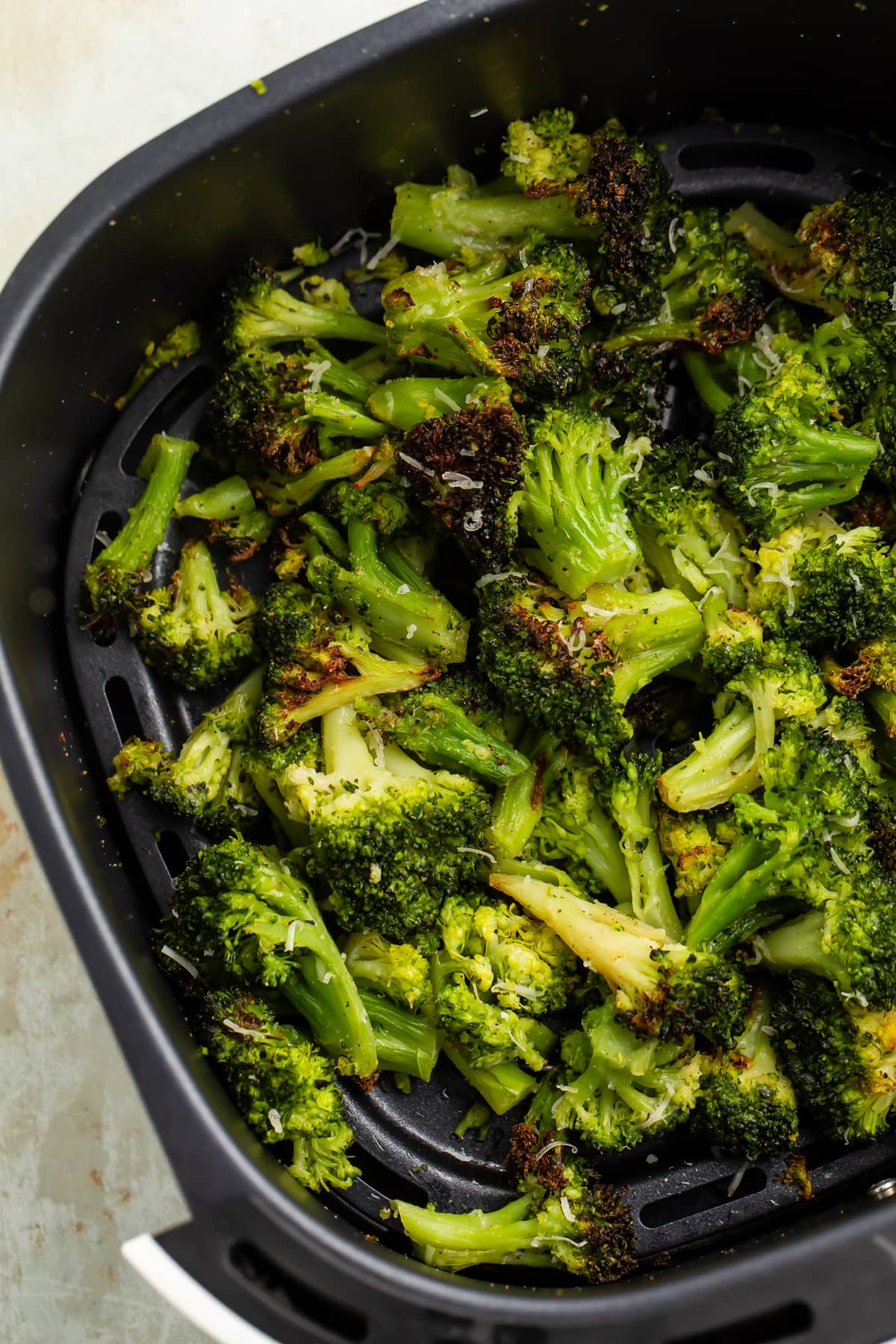 Previously frozen broccoli florets, resting in an air fryer basket after being cooked until some spots are dark brown and crisp.