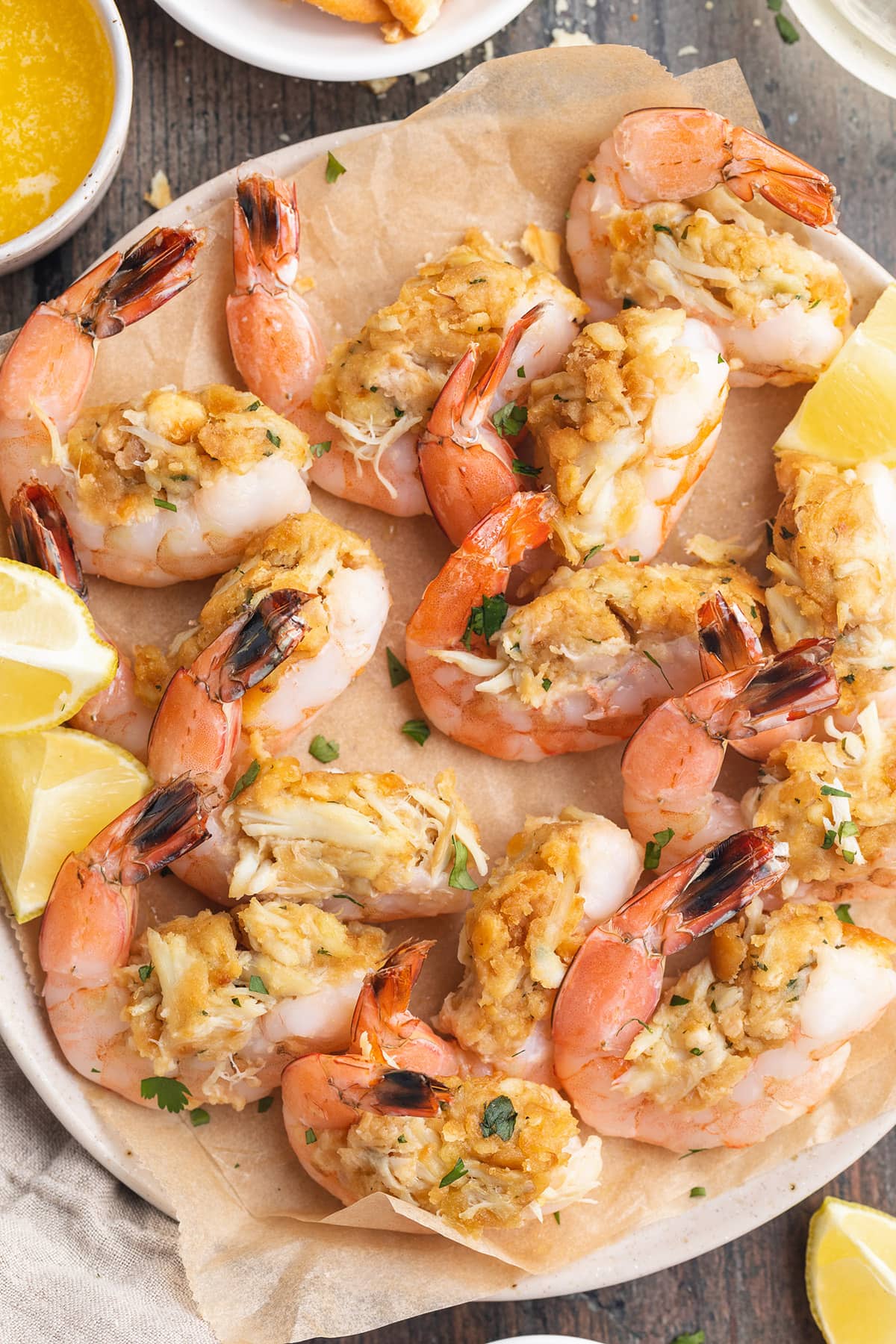 Top-down photo of a plate of baked, stuffed shrimp with lemon wedges and fresh herbs.