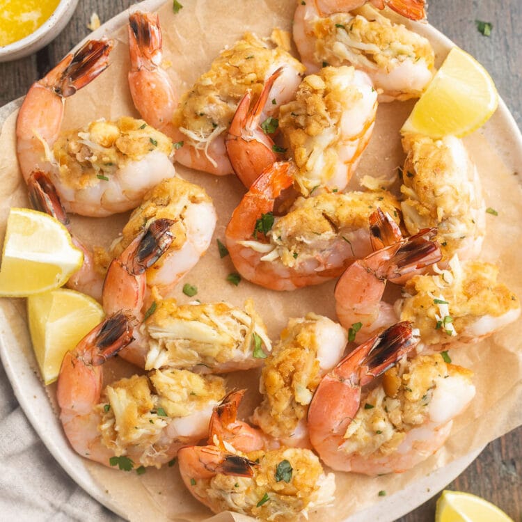 Top-down photo of a plate of baked, stuffed shrimp with lemon wedges and fresh herbs.