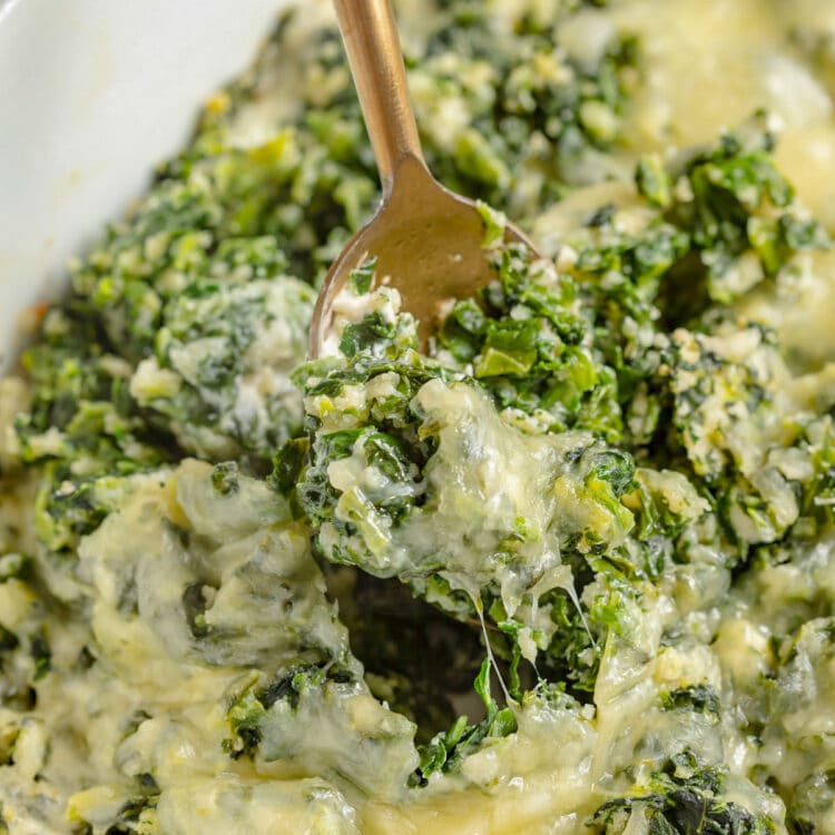 Cheesy parmesan spinach casserole being scooped out of a casserole dish with a gold spoon.