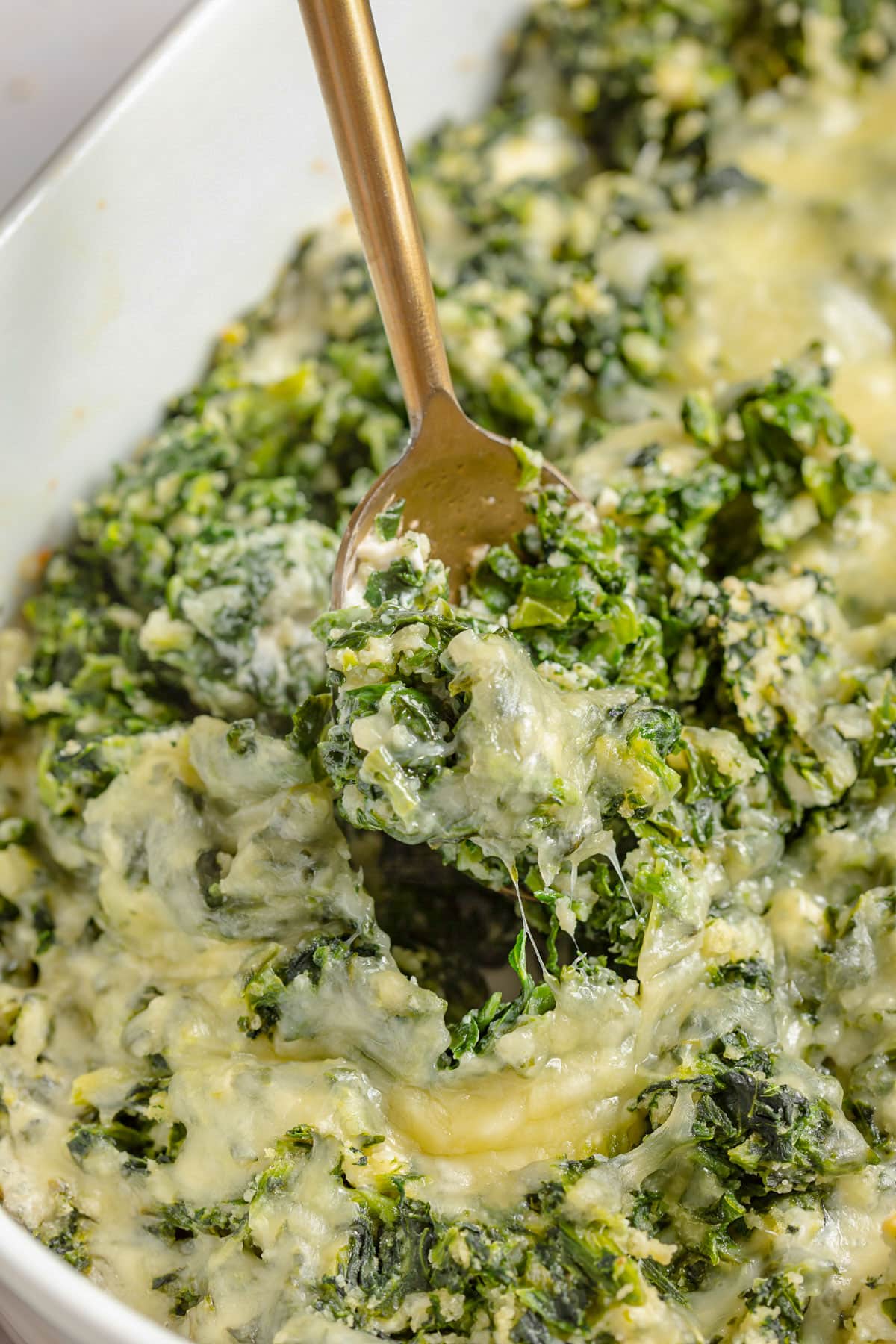 Cheesy parmesan spinach casserole being scooped out of a casserole dish with a gold spoon.