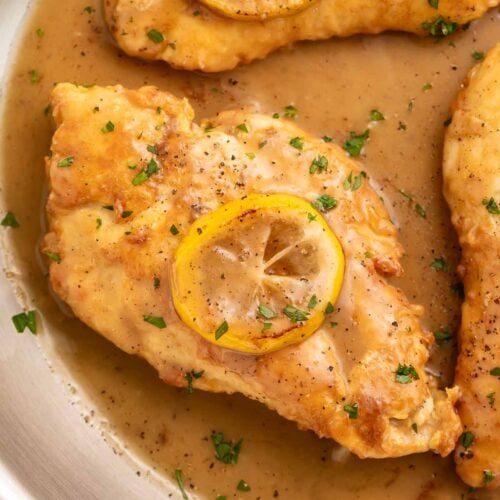 Lightly pan-fried Chicken Francese in a large skillet with lemon sauce, topped with a sautéed lemon coin.