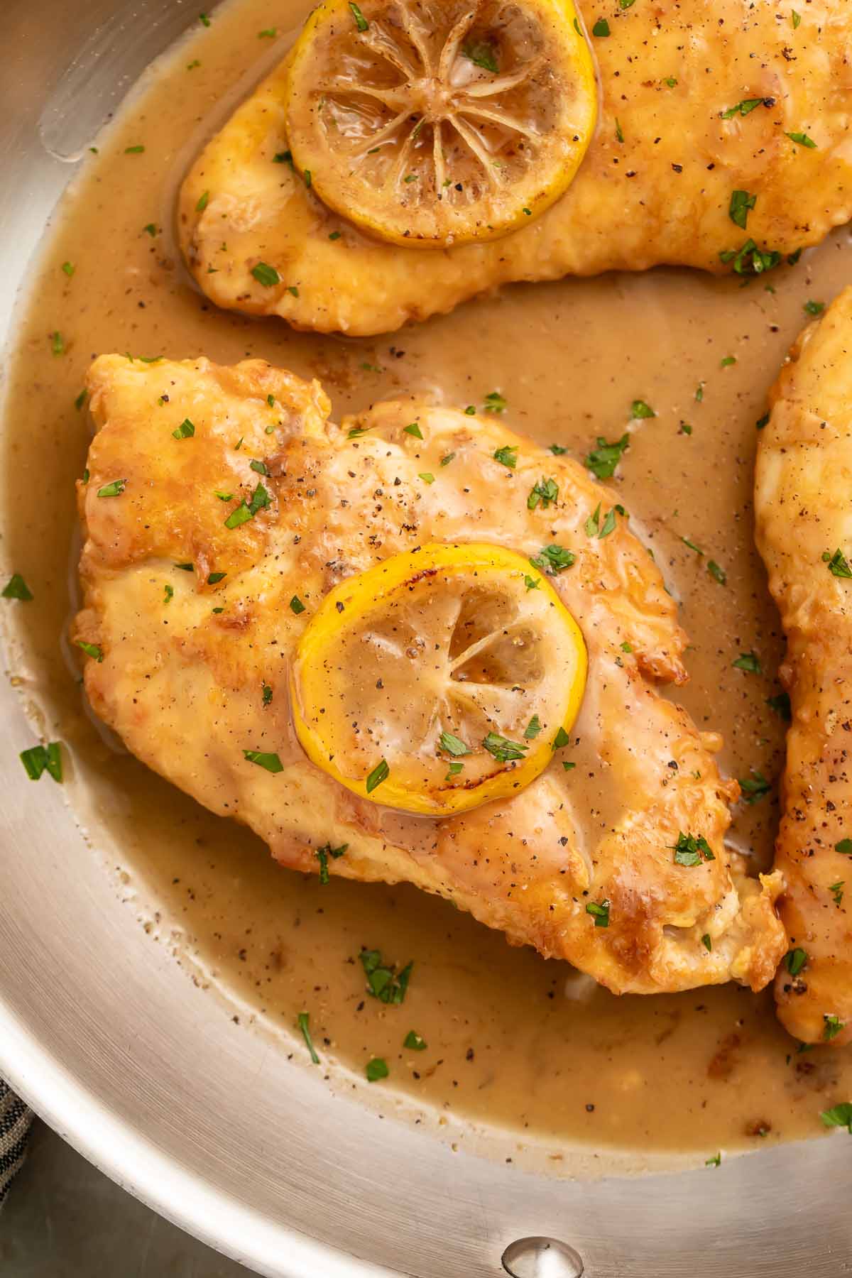 Lightly pan-fried Chicken Francese in a large skillet with lemon sauce, topped with a sautéed lemon coin.