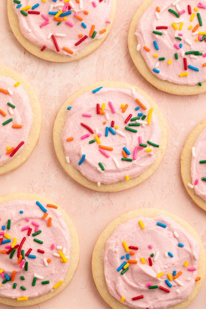 Rows of gluten free sugar cookies topped with pink buttercream frosting and rainbow jimmies on parchment paper.