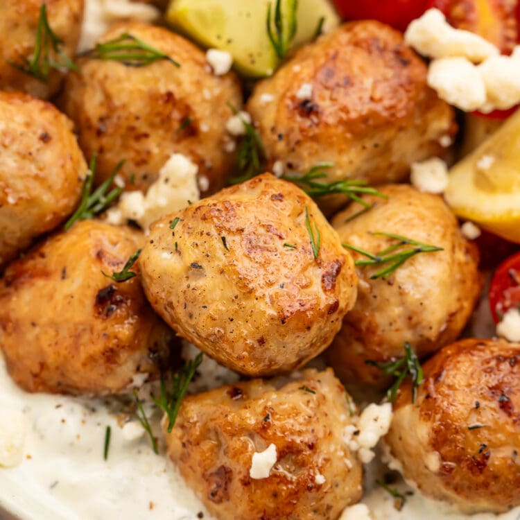 Close-up of Greek chicken meatballs in a large bowl with rice and veggies.