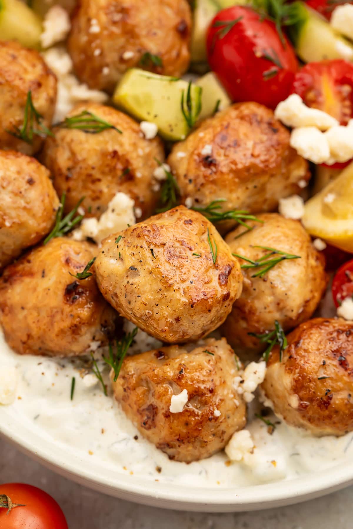 Close-up of Greek chicken meatballs in a large bowl with rice and veggies.