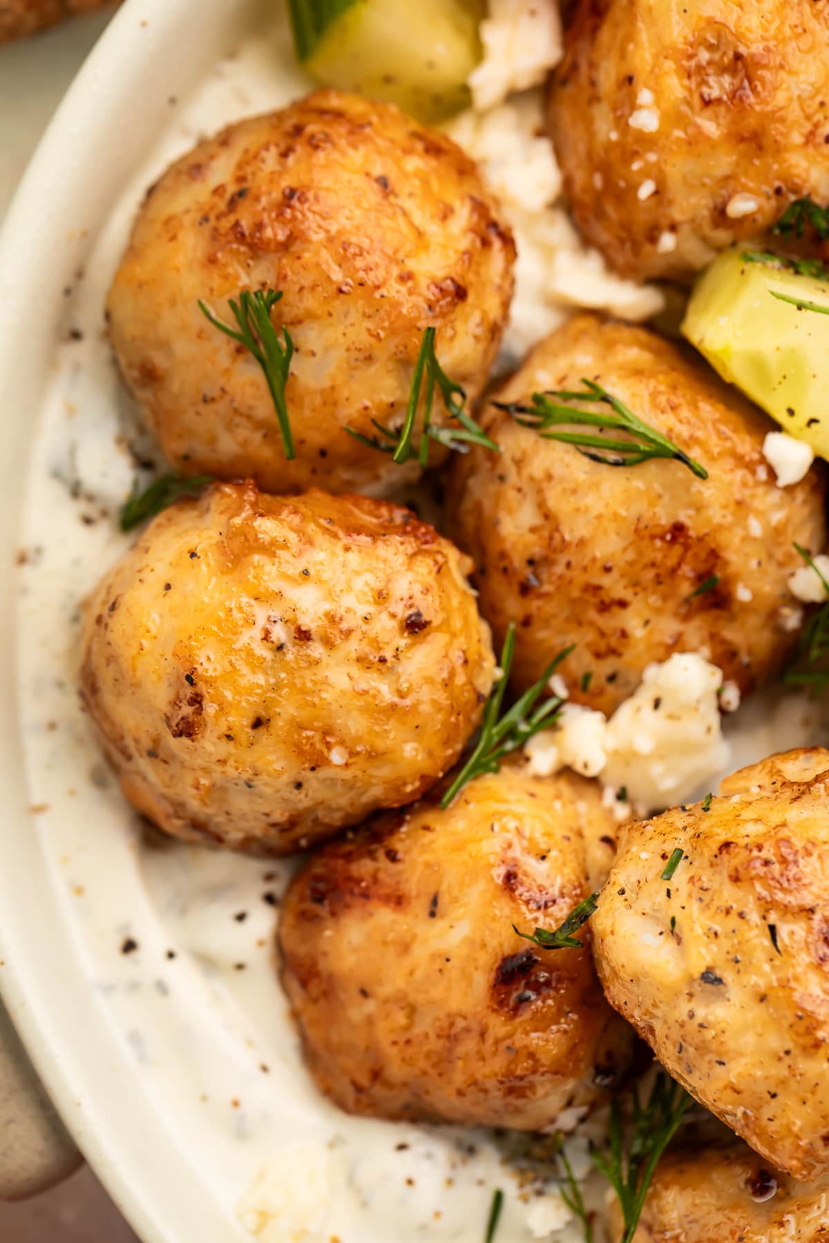 Close-up of greek chicken meatballs in a large bowl with rice and veggies.