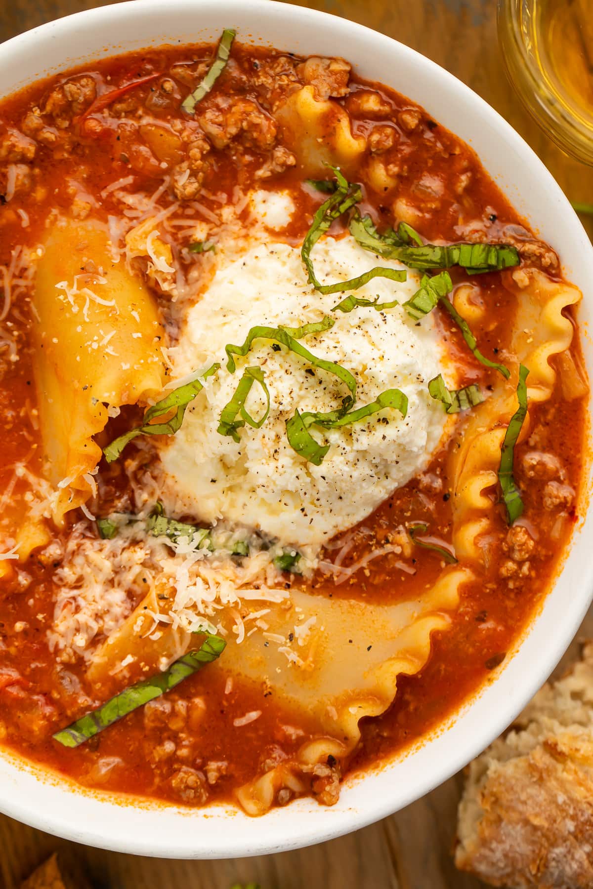Close-up of lasagna soup in a large white bowl on a wooden table.