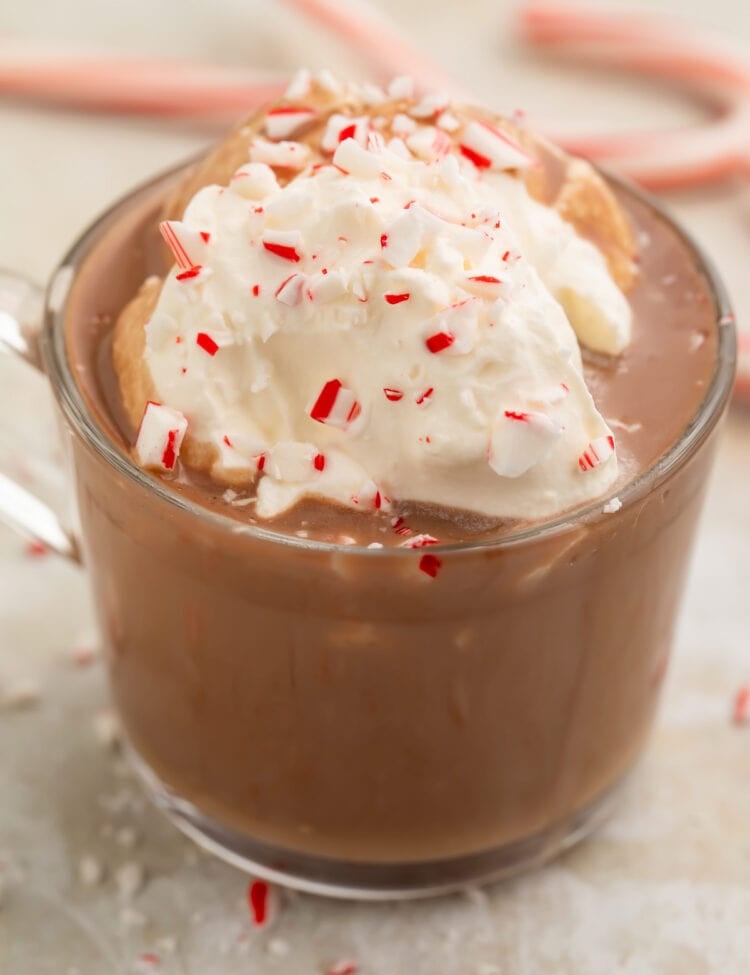 A clear glass mug of rich paleo peppermint hot chocolate topped with whipped coconut cream and candy cane pieces.