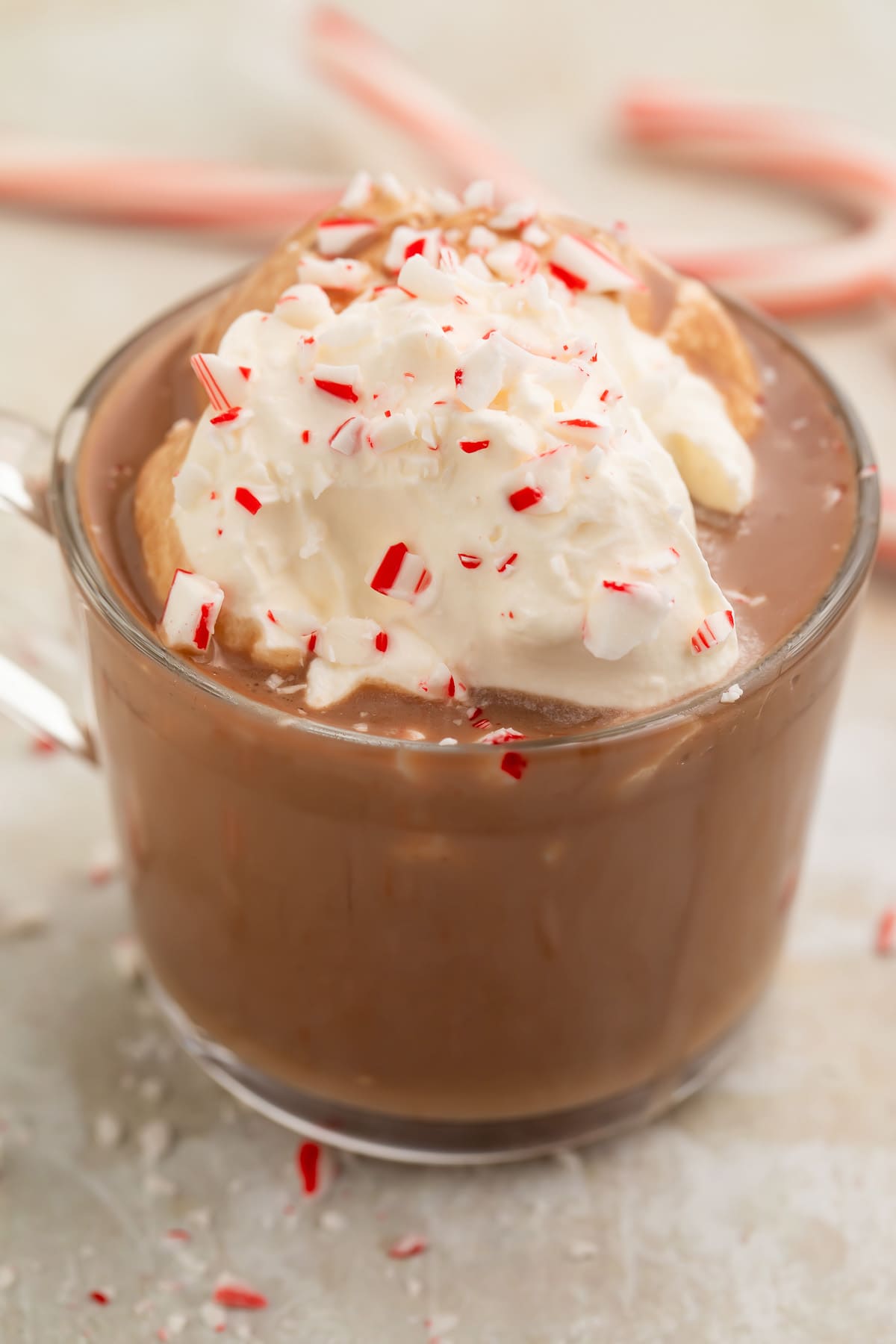 A clear glass mug of rich paleo peppermint hot chocolate topped with whipped coconut cream and candy cane pieces.
