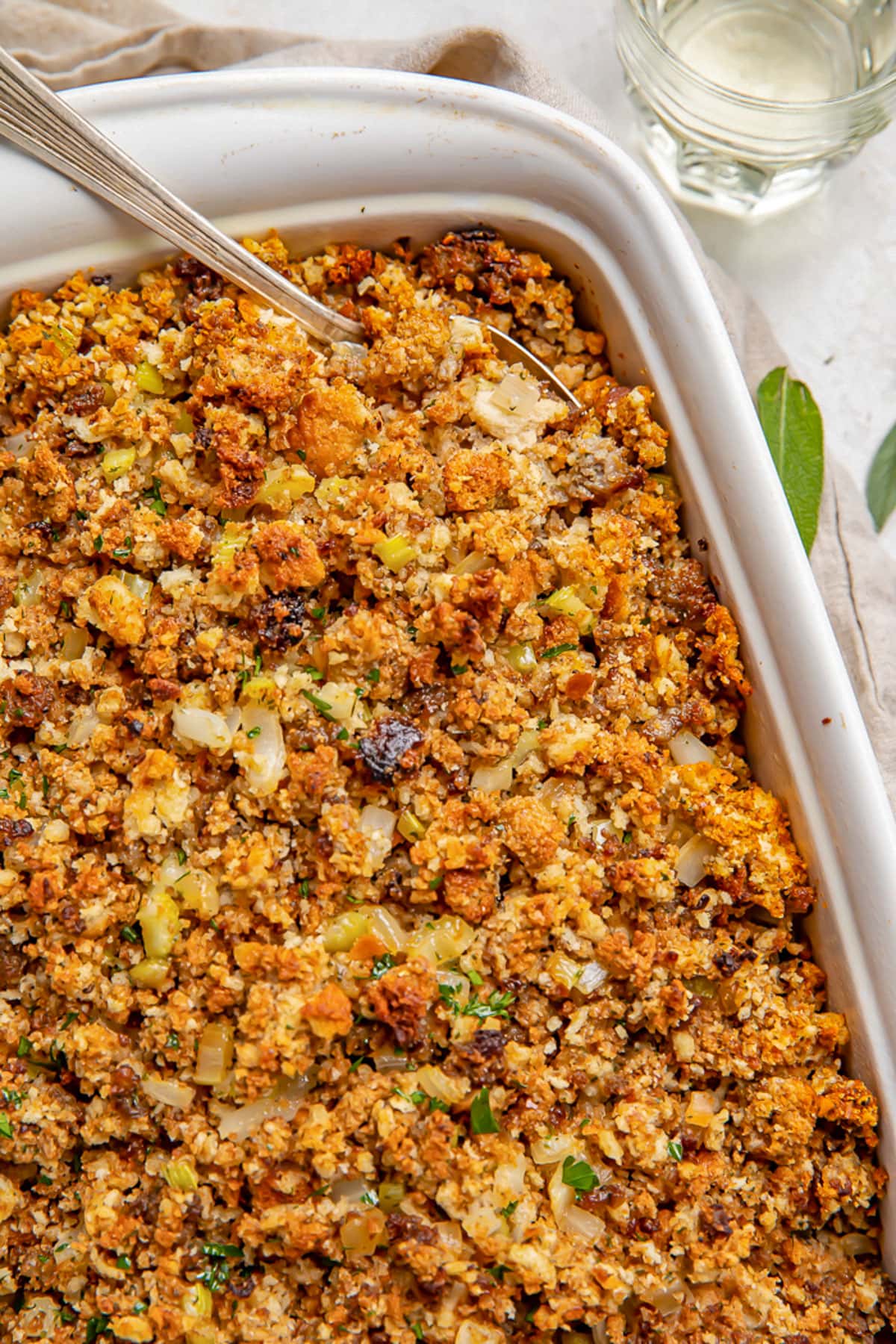 Sausage stuffing in a white rectangular casserole dish with a large spoon.