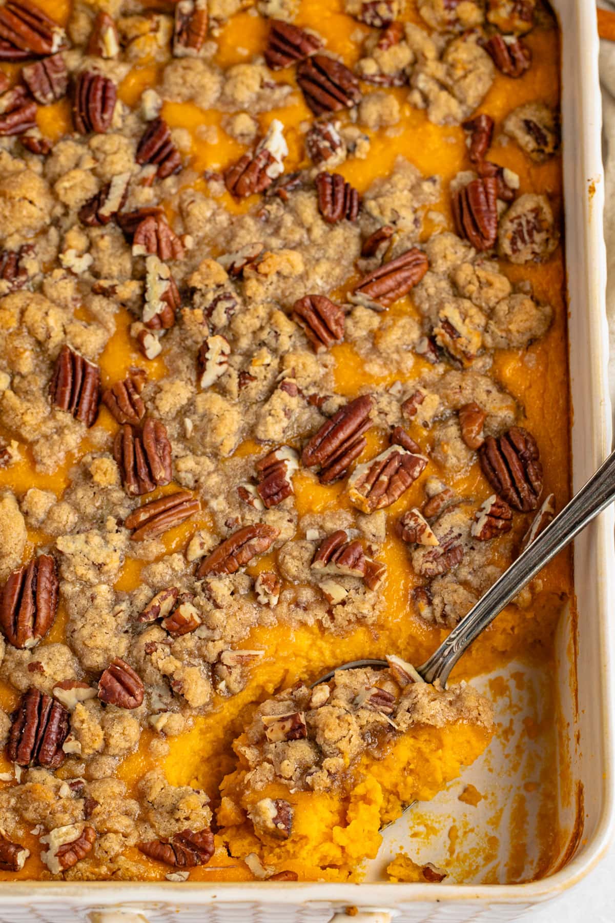 A large pan holding sweet potato pudding topped with pecans with a spoonful of pudding taken out of the pan.