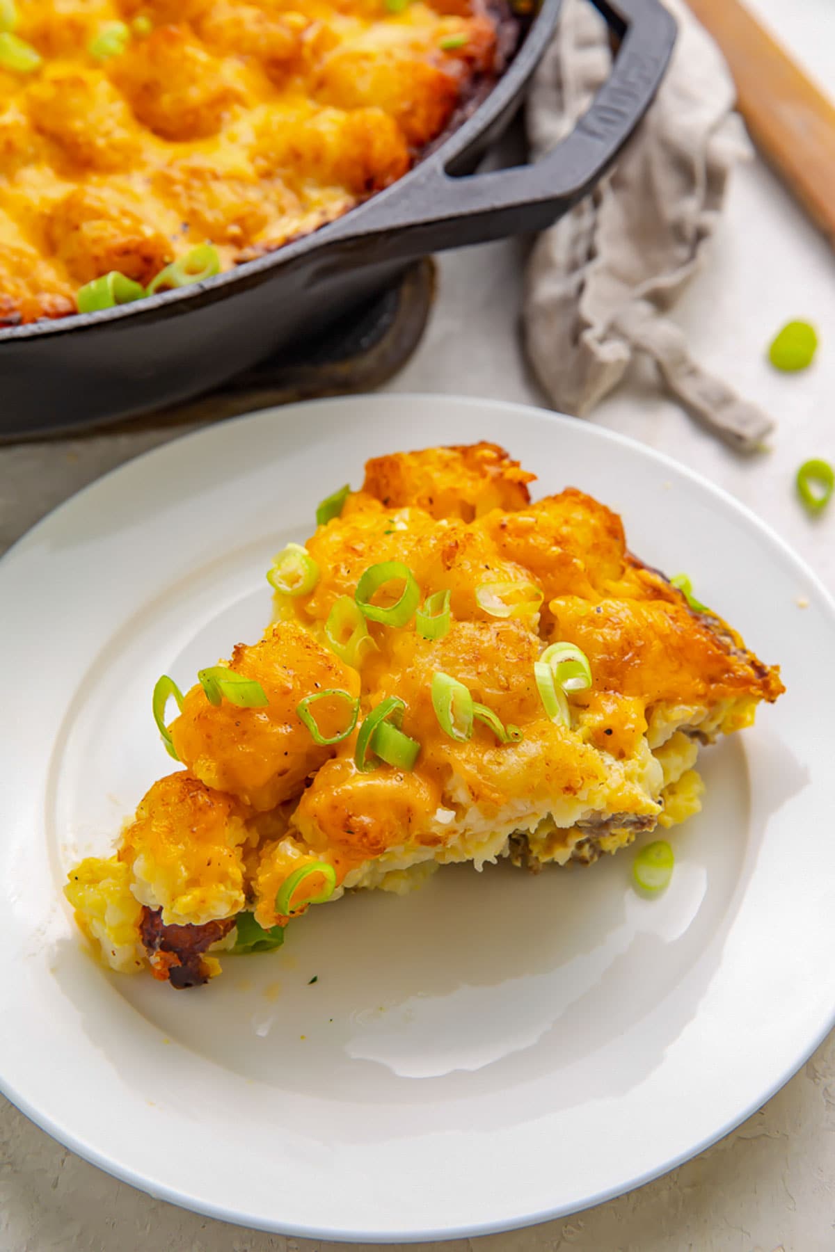 A triangular wedge of tater tot breakfast casserole on a white plate.