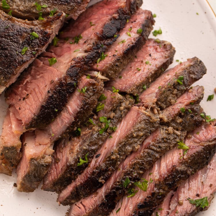 Overhead photo of sous vide chuck roast on a white platter, with half the chuck roast sliced into thin strips and fanned out to show the crust and the inside of the roast.