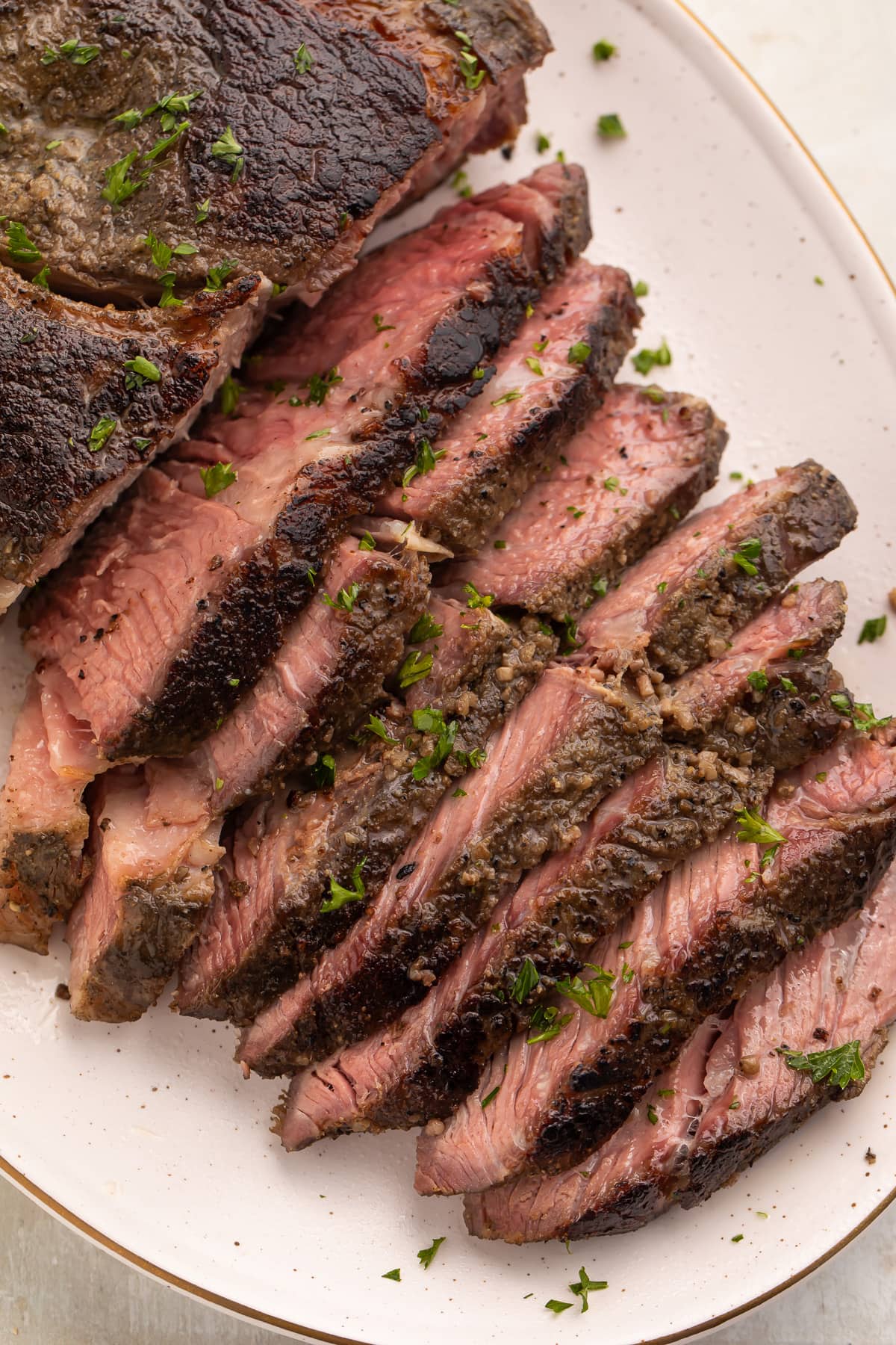 Overhead photo of sous vide chuck roast on a white platter, with half the chuck roast sliced into thin strips and fanned out to show the crust and the inside of the roast.